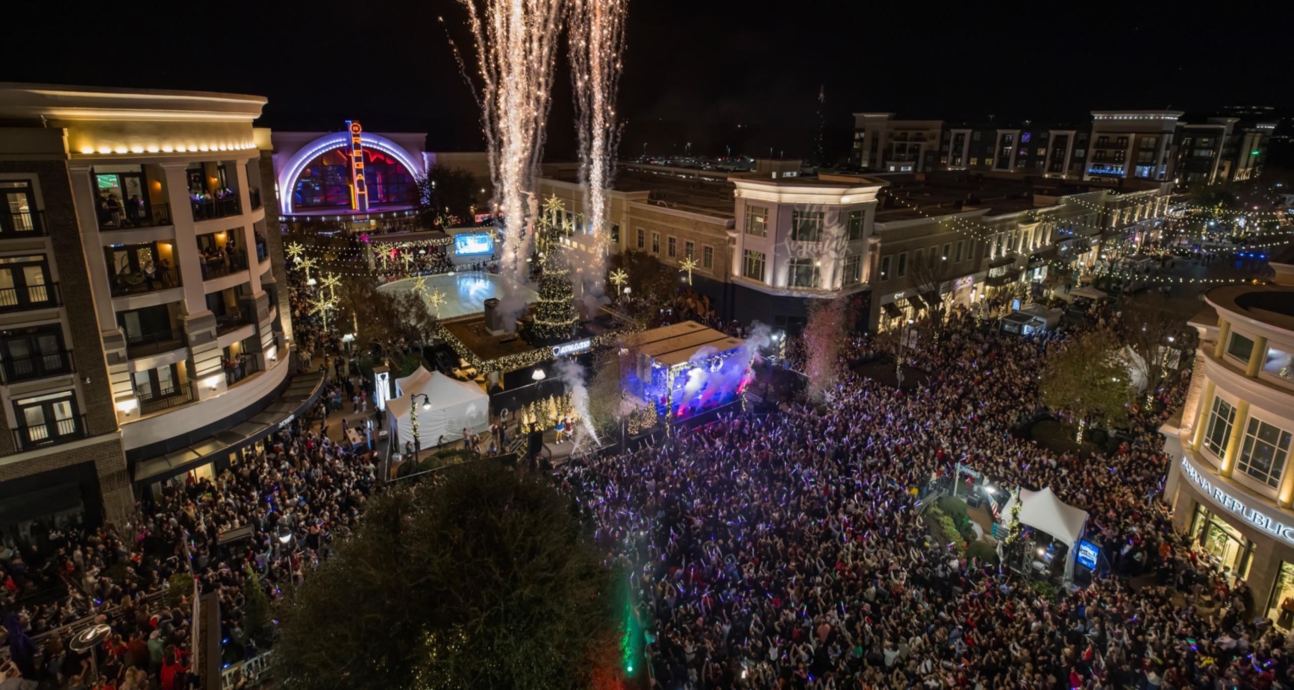 A massive crowd watches fireworks above the lit Christmas tree in an outdoor area at Avalon