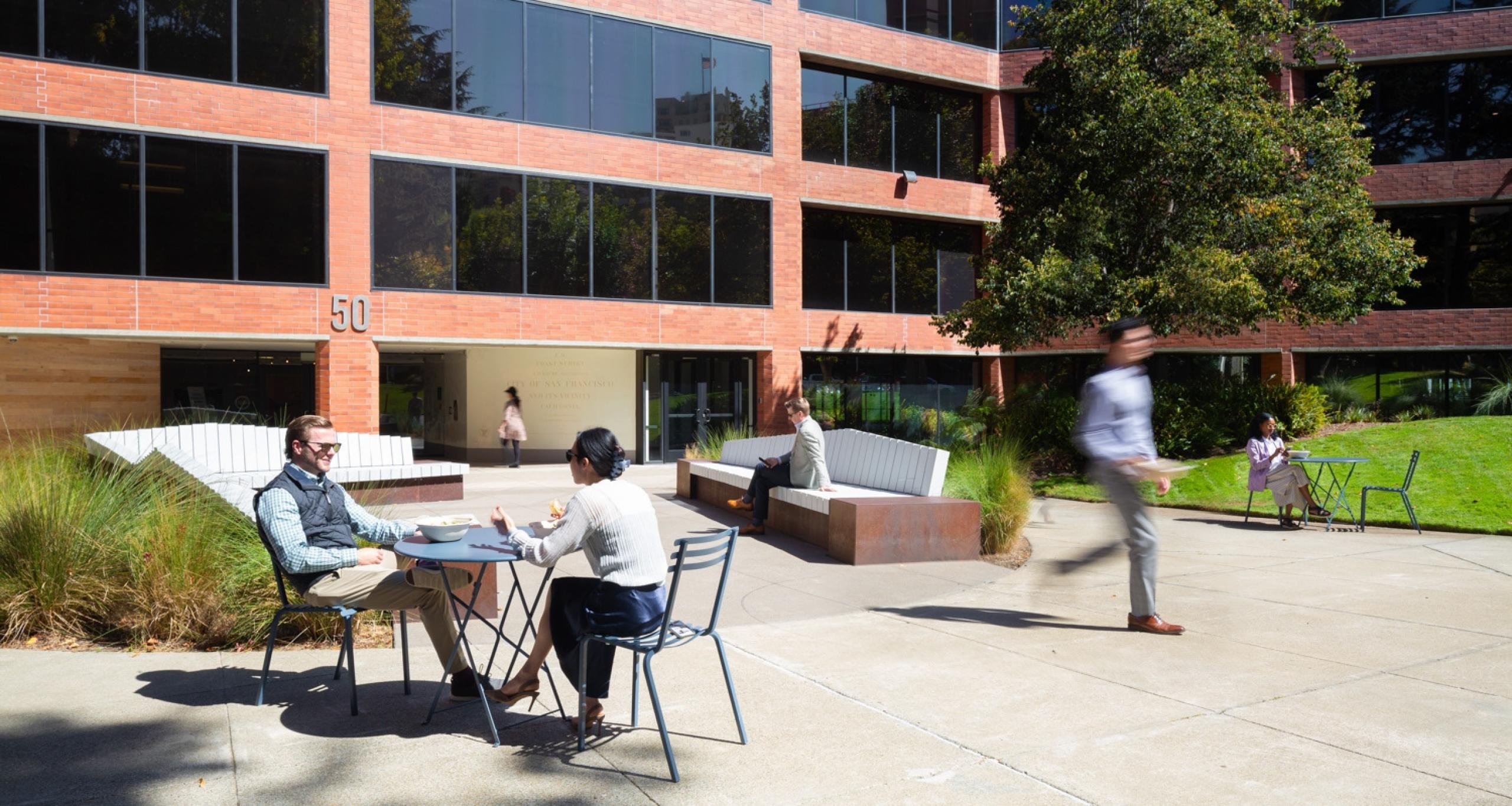 Visitors sitting at tables and benches and walking in Waterfront Plaza's exterior courtyard